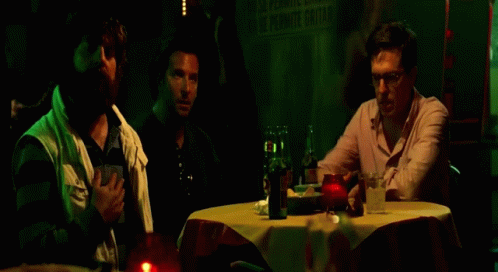 three men stand around a table in the dark