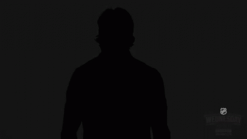 a man standing in the dark holding a tennis racquet