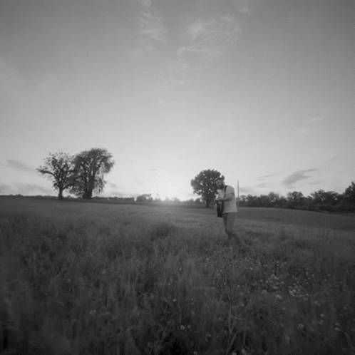 black and white image of a person walking through an open field