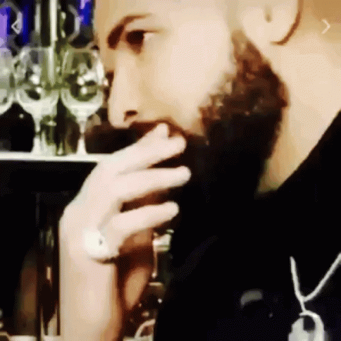 a bearded man is drinking a wine glass in a bar