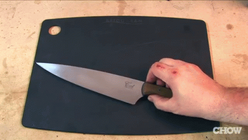 a hand with a sharp knife on a brown  board