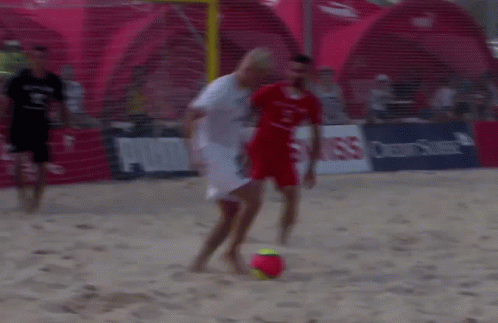 two men playing soccer in the sand outside