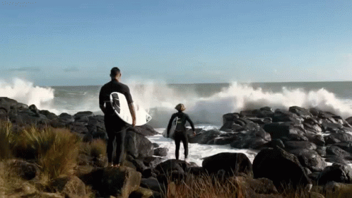 two people walking away from the ocean carrying surfboards