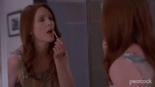 a woman with makeup brushes her teeth in the mirror