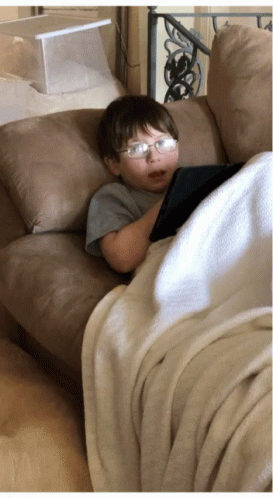 small child with glasses and nose paint lying on the back of a couch