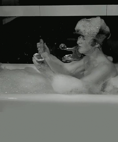 a man sitting in a bath tub while taking a shower