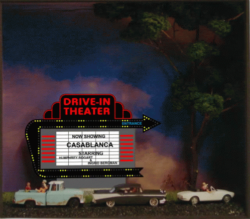two cars driving past a large drive - in theatre sign