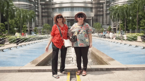 two women with sun glasses are standing near the fountain in an artistic looking building