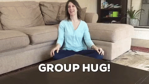 a woman with long dark hair is sitting on the floor in front of a coffee table and couch that says group hug