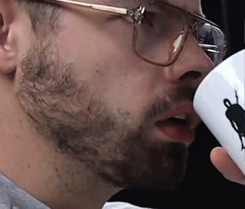 a man drinking from a coffee cup while wearing glasses