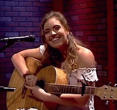a girl is holding an acoustic guitar while singing