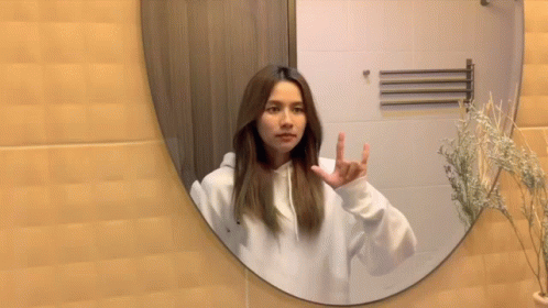 a woman standing in front of a mirror making an odd hand sign