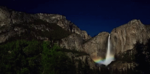 waterfall with rainbow coming out from it into the sky