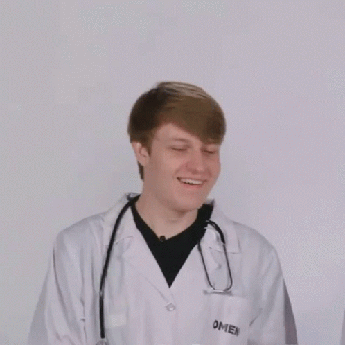 a young male doctor wearing a lab coat, standing and holding his arms around the desk