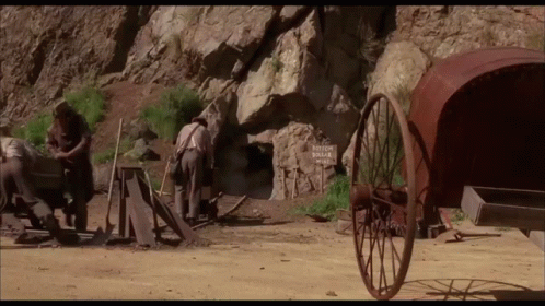 a group of men hing wooden wheels through an empty mountain area