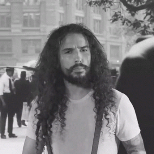 a man with long curly hair and suspenders walking down a street