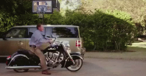 a man standing on top of a motorcycle next to a car