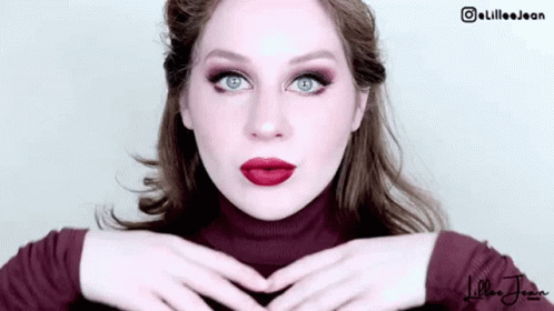 a woman wearing a white and purple makeup holding her hands over the face