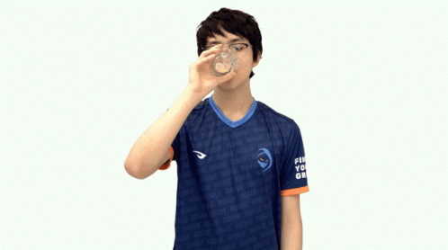 a boy drinking from a glass while standing against a white background