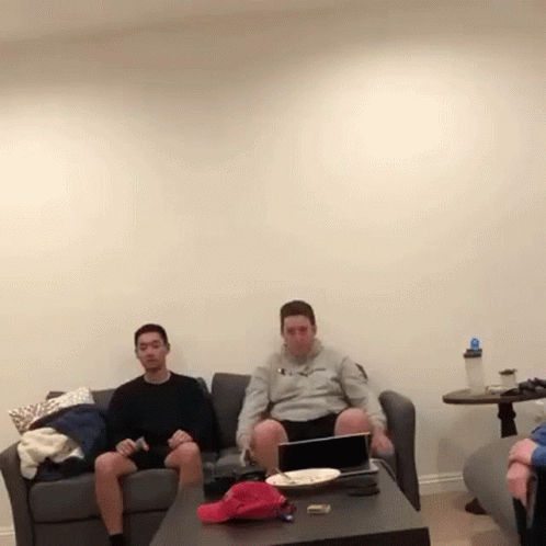 three men sitting on couches and watching soing on a television