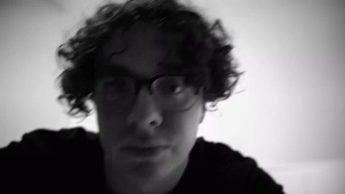 a man wearing glasses with the background of a pograph blurred