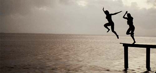 two people jump off a dock into the ocean