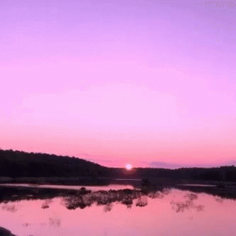 an empty lake with hills and sun setting