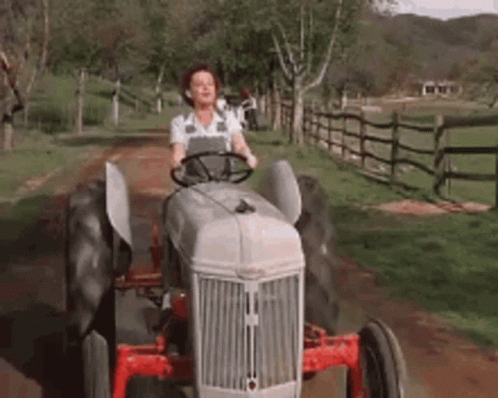 a woman with an apron on drives an old - fashioned tractor