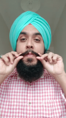 a man in a checkered shirt and turban puts on his hair with one hand