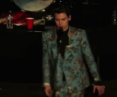 a man is wearing a floral suit and holds a microphone
