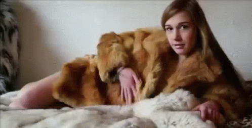 a woman sitting on top of a bed with a fur jacket