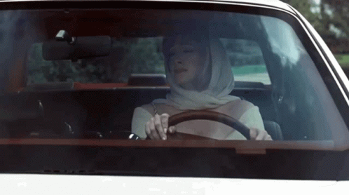 an old po of a woman driving a car with head scarf on