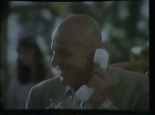 an old black man talking on a telephone while wearing a blue jacket