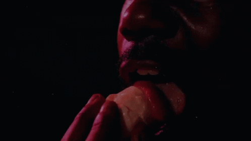 a man with a purple face and black background eating an orange