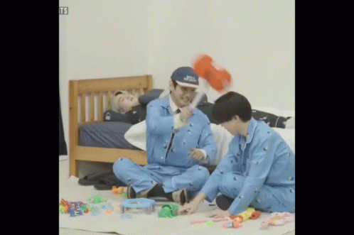two men sitting on a bed near a plastic penguin