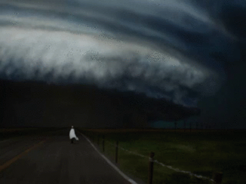 the storm approaches and a person is walking down the road