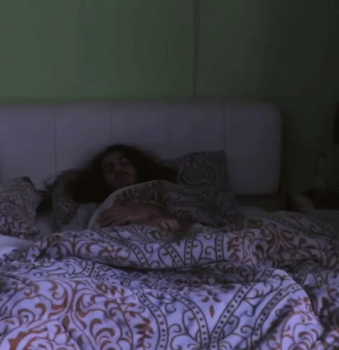 a woman hiding under blankets on a bed