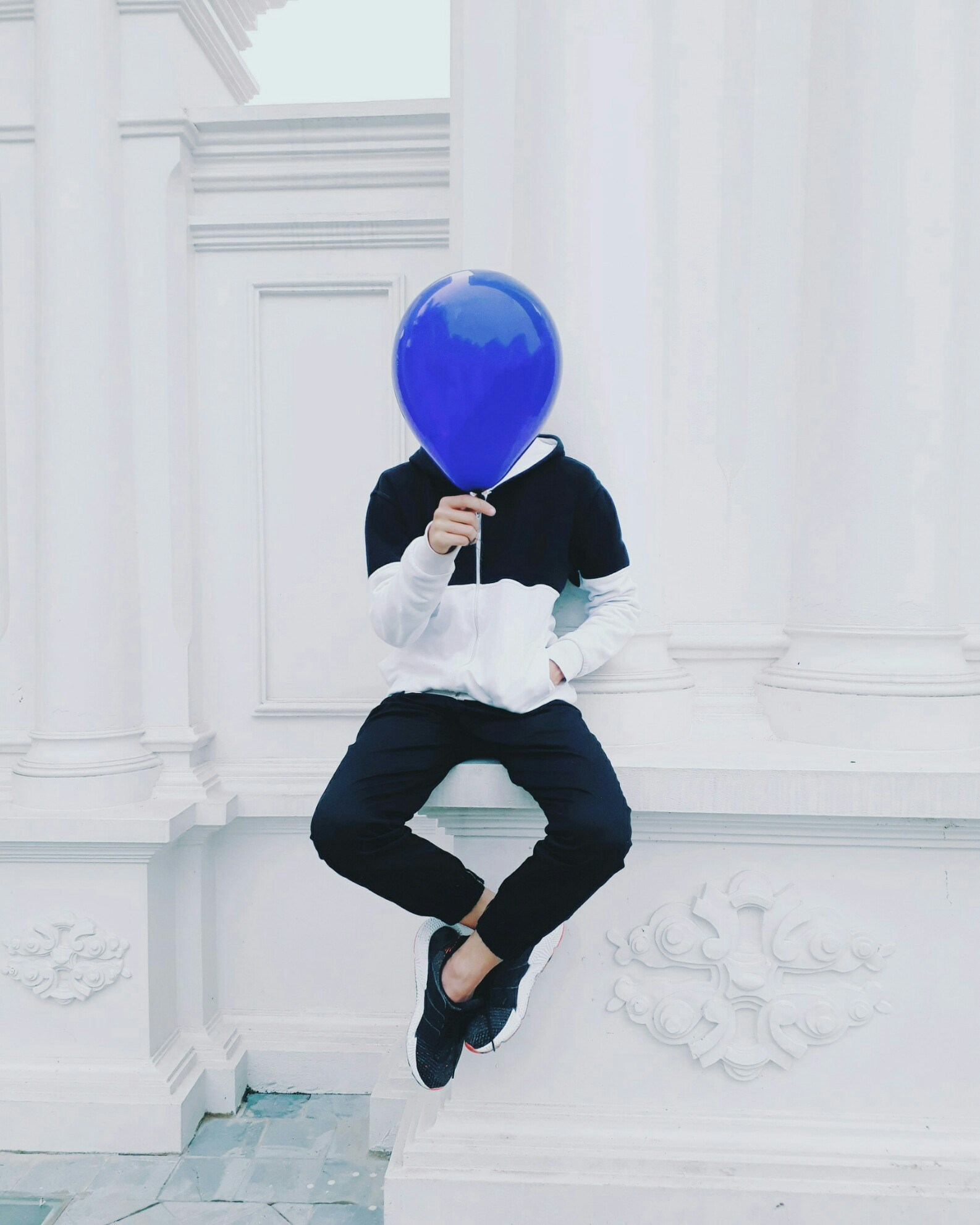 a person with a blue balloon is posed on a pillar