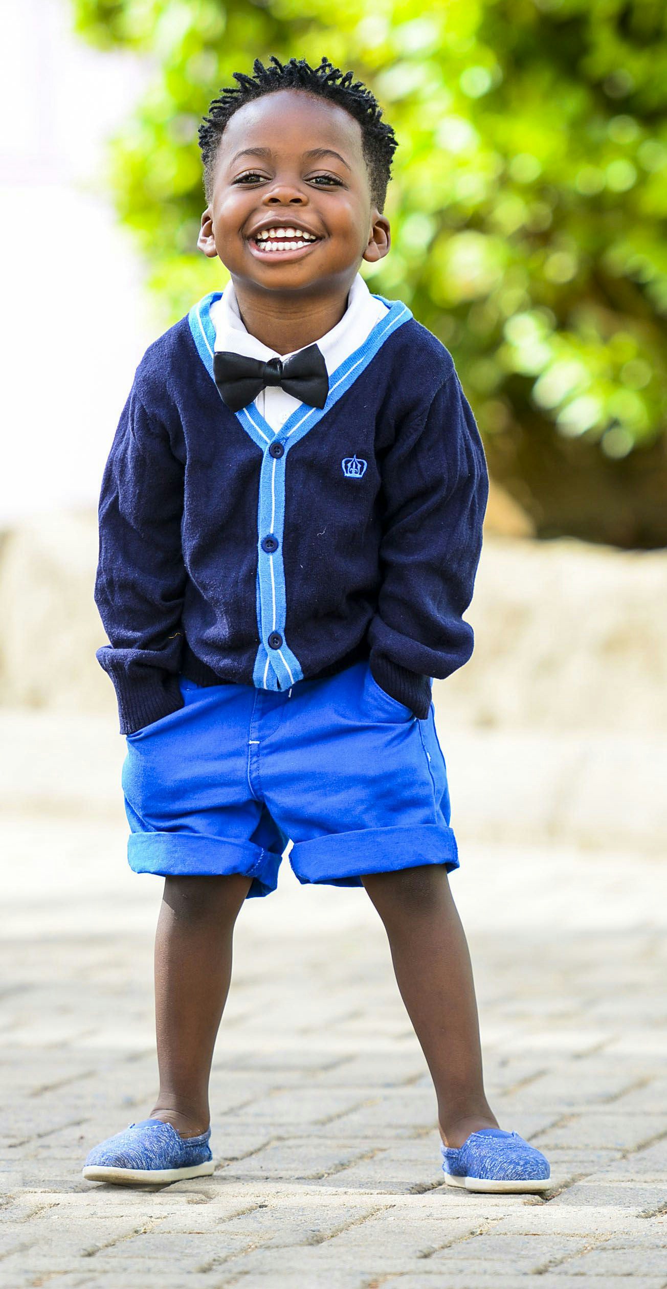 a child stands with his legs crossed while wearing blue shorts