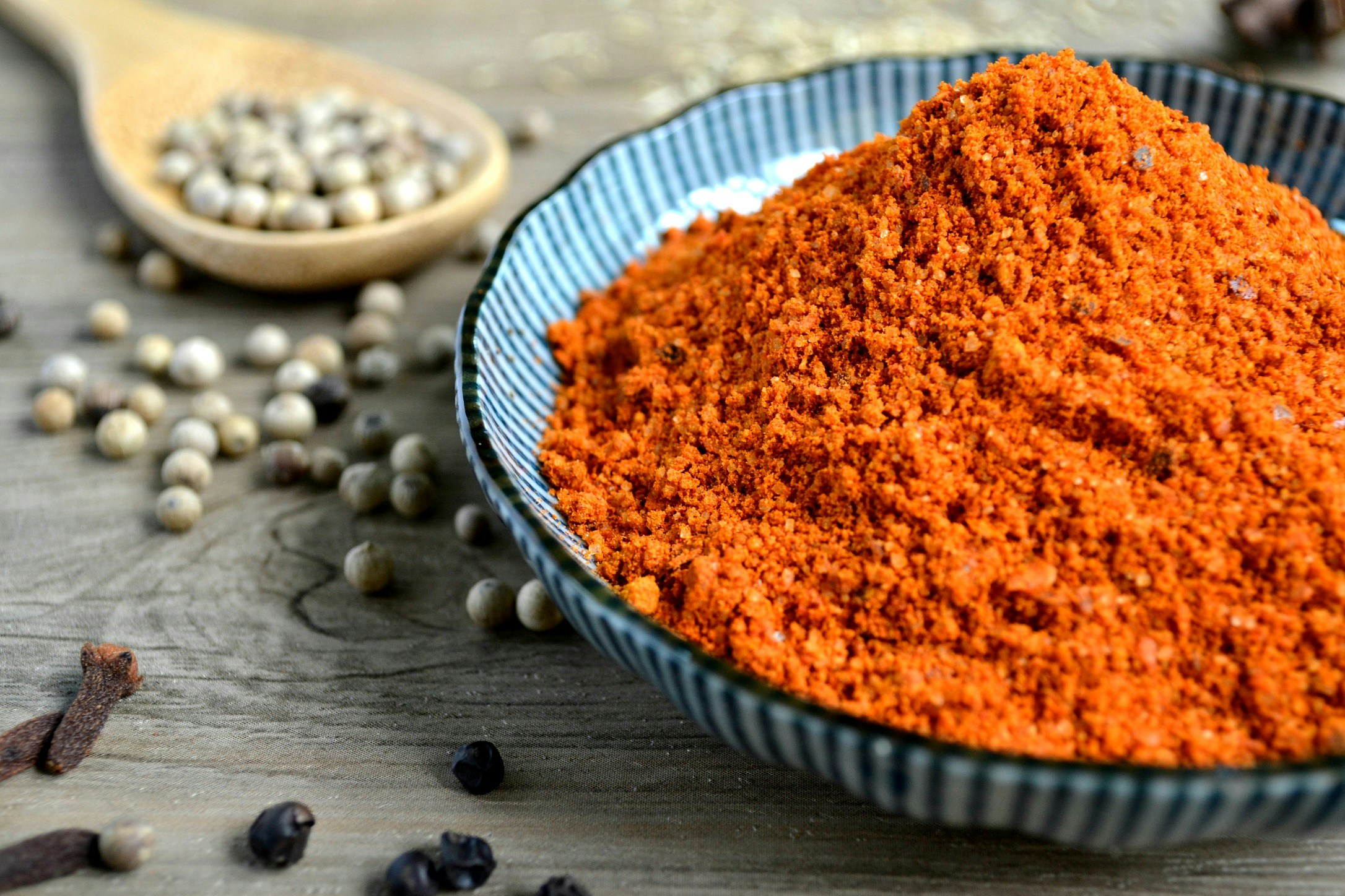 a bowl of red spice is next to a spoon and seed pods