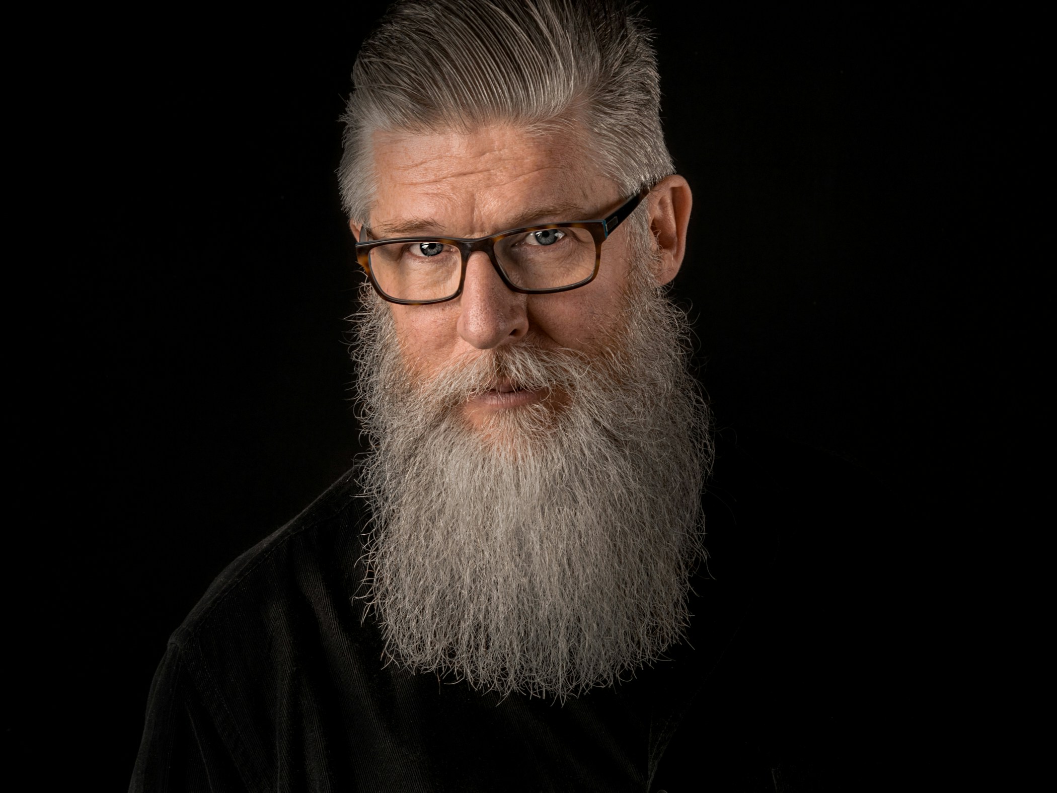 a bald, bearded man with glasses on looking serious