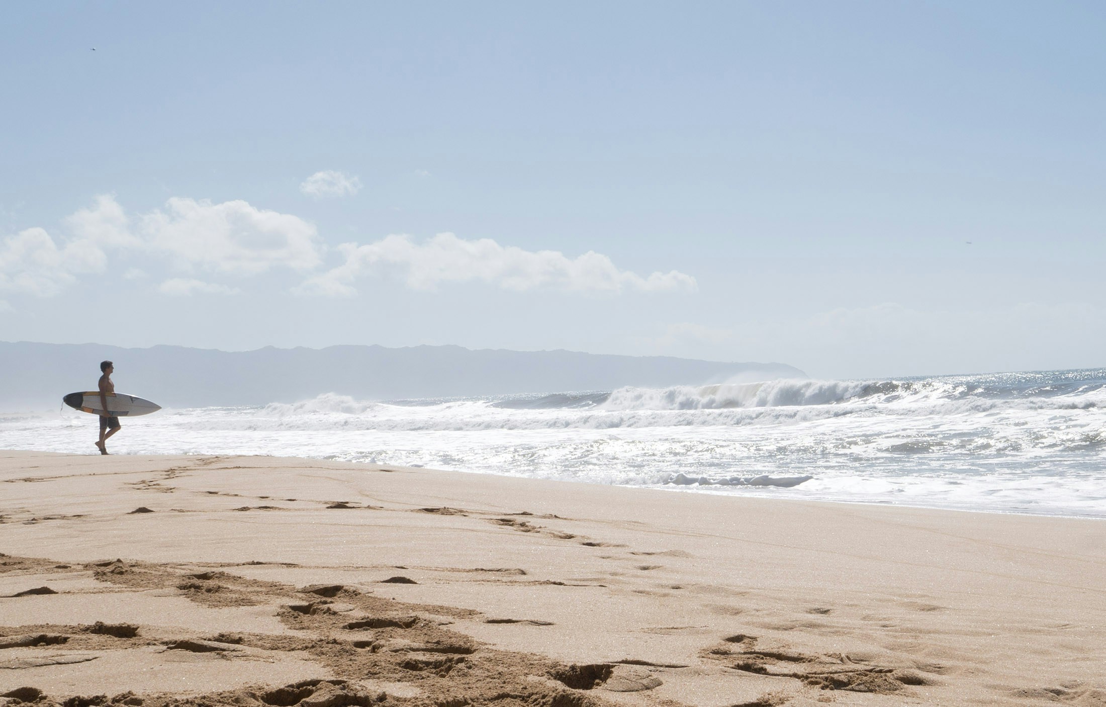 a lone man holding a surfboard walks towards the water