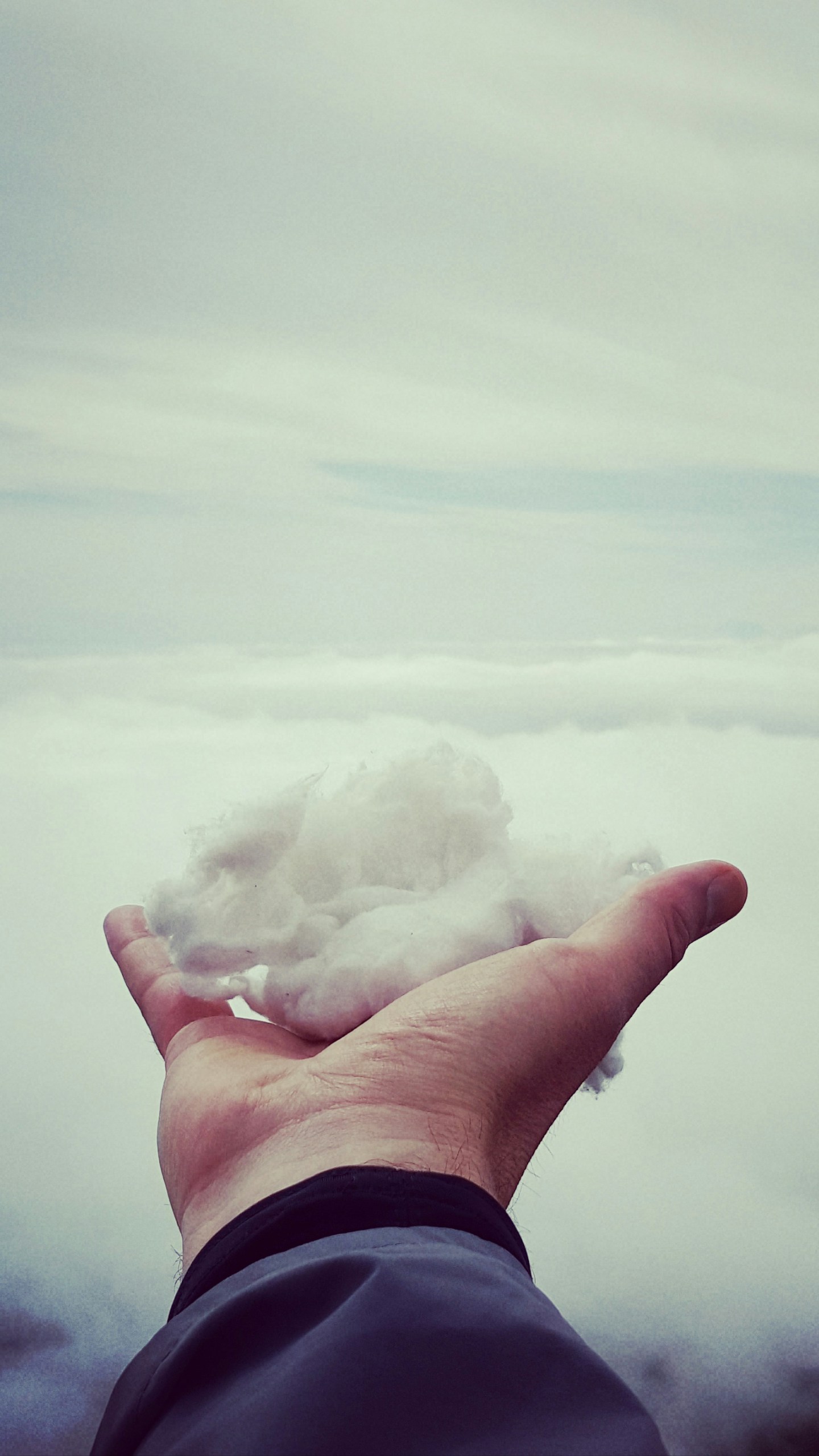 a hand is holding some white substance above the clouds