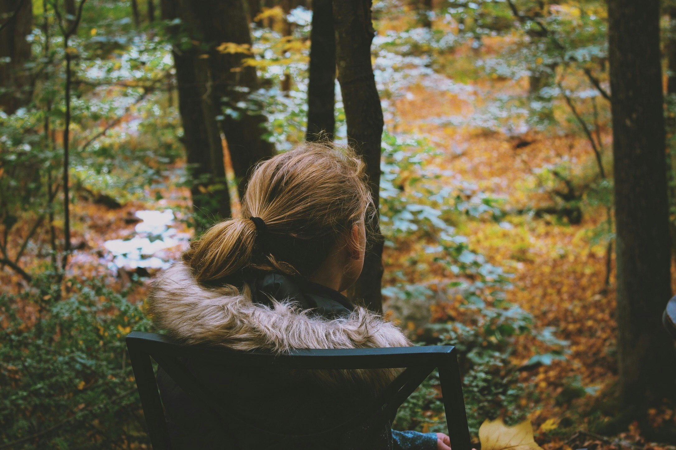 a young woman sitting on a wooden chair looking at trees