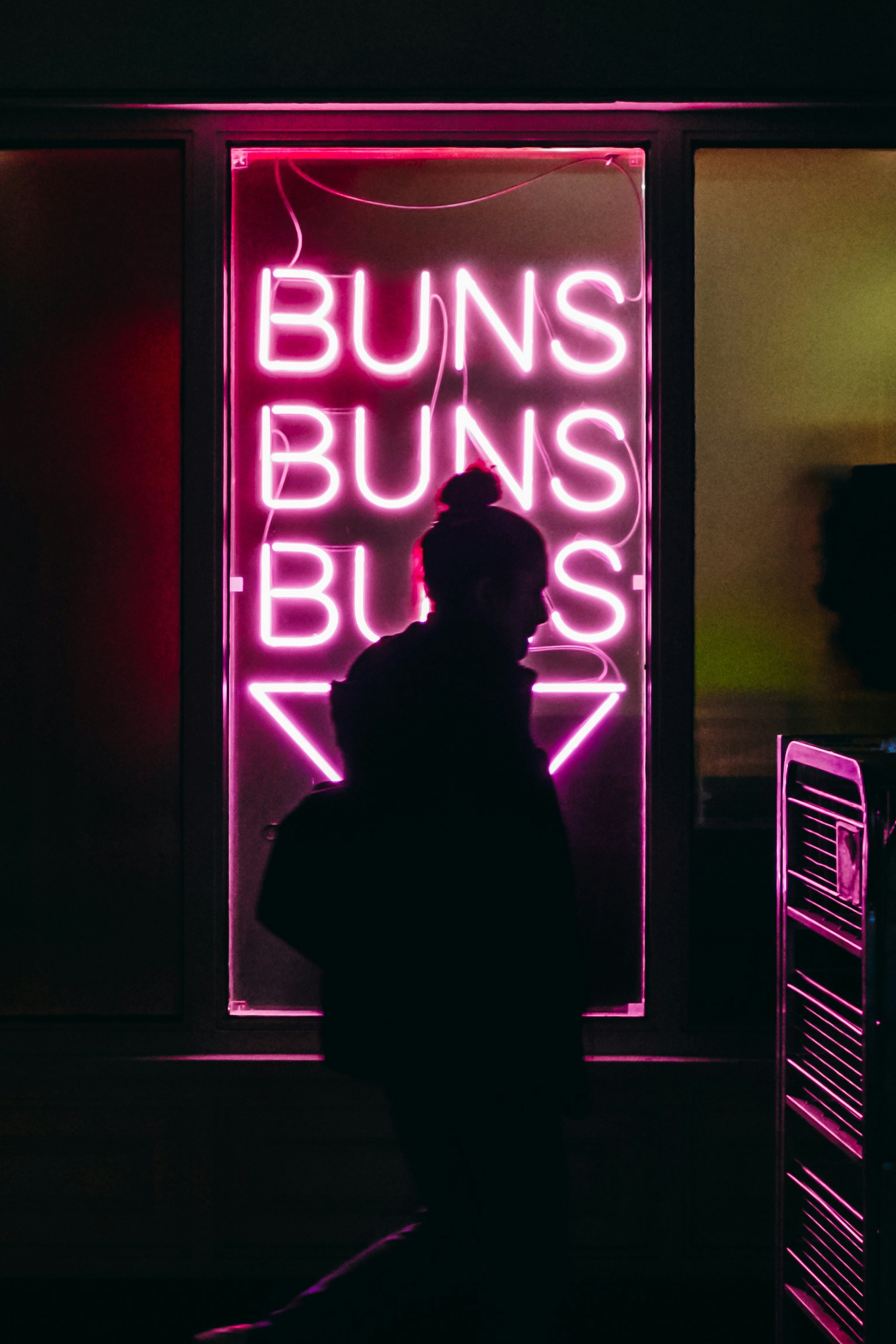 a man standing in front of a neon sign that reads buns guns blues